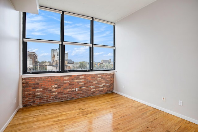 empty room featuring baseboards, brick wall, and wood-type flooring