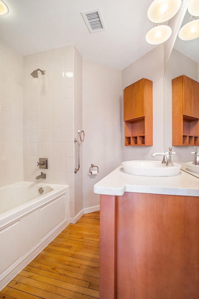 bathroom with shower / bathtub combination, wood-type flooring, vanity, baseboards, and visible vents
