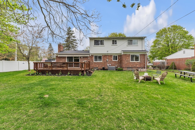 back of property featuring a wooden deck, an outdoor fire pit, a yard, brick siding, and a fenced backyard