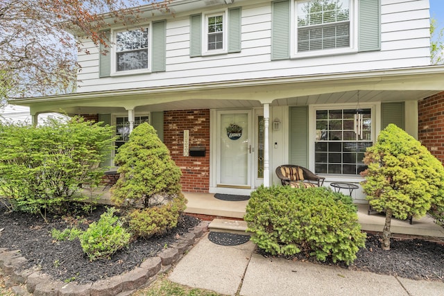 doorway to property featuring covered porch and brick siding