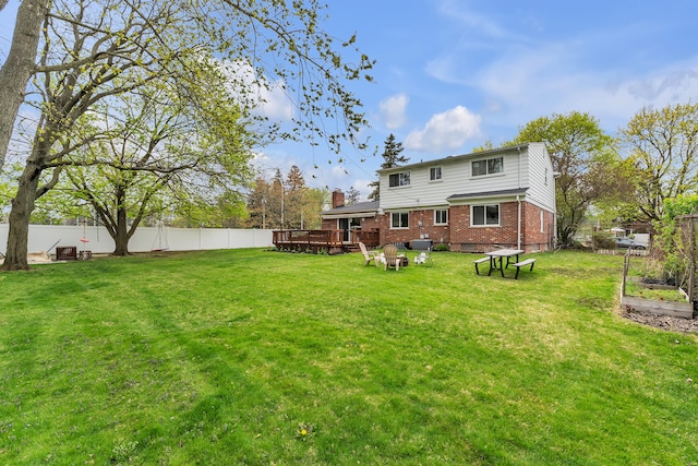 back of house featuring a deck, a fenced backyard, a garden, brick siding, and a lawn