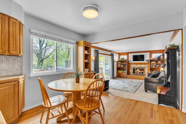 dining area with baseboards, light wood-style flooring, and a glass covered fireplace