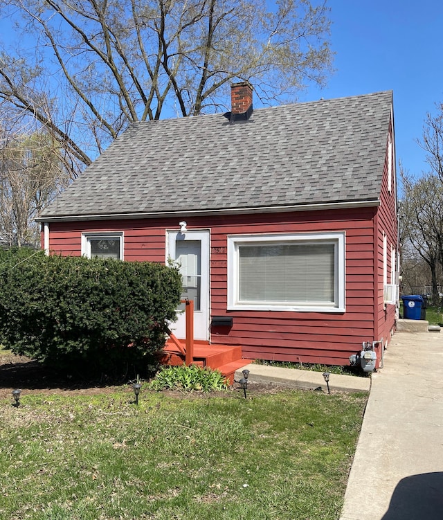 view of front of house with cooling unit, a front yard, a shingled roof, and a chimney