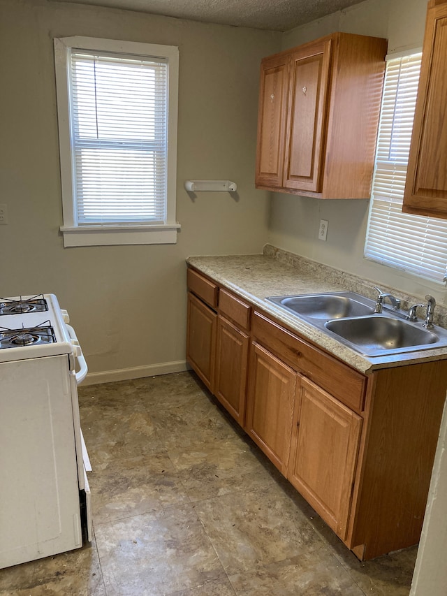 kitchen with gas range gas stove, brown cabinetry, light countertops, a sink, and baseboards