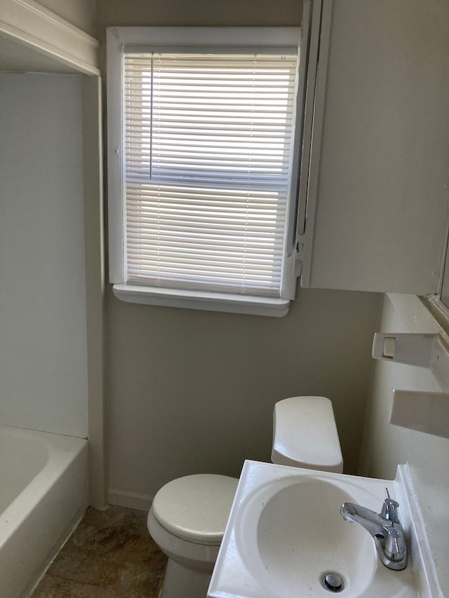 full bathroom with toilet, a sink, a tub to relax in, and baseboards