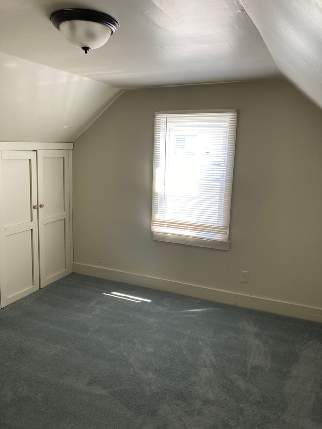 bonus room with dark carpet, lofted ceiling, and baseboards