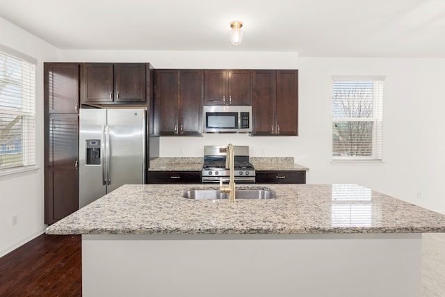 kitchen with dark wood-style floors, stainless steel appliances, dark brown cabinets, and an island with sink