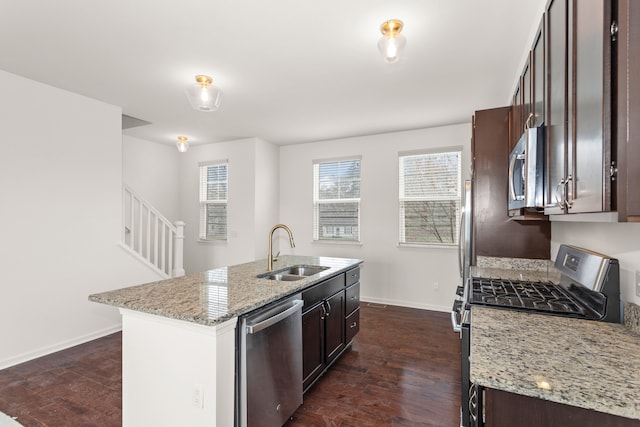 kitchen featuring a sink, stainless steel appliances, dark brown cabinetry, baseboards, and a center island with sink