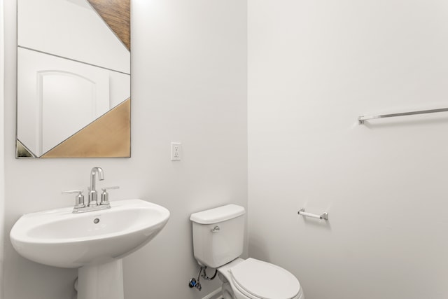 half bath featuring baseboards, toilet, and a sink