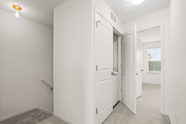 hallway with an upstairs landing, visible vents, light colored carpet, and baseboards