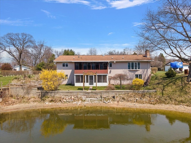 back of house with a lawn, a water view, a chimney, and a sunroom