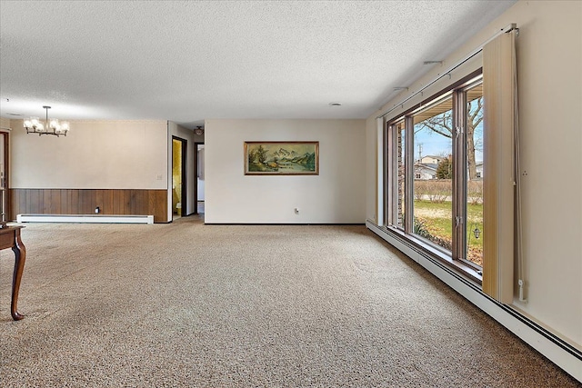 carpeted spare room with wainscoting, baseboard heating, a textured ceiling, a baseboard heating unit, and a notable chandelier