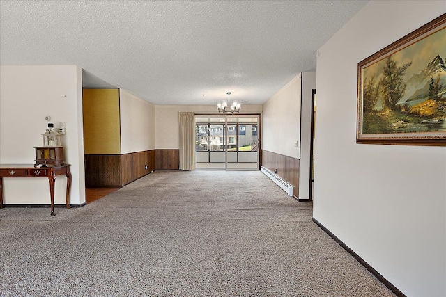 unfurnished room with a textured ceiling, baseboard heating, wainscoting, carpet floors, and an inviting chandelier