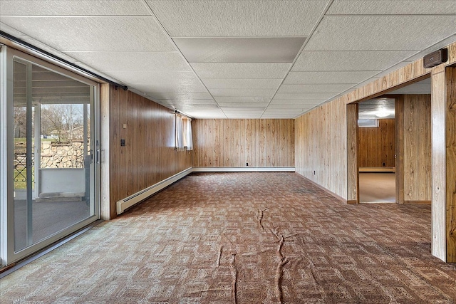 empty room featuring baseboards, wooden walls, baseboard heating, a paneled ceiling, and a baseboard heating unit