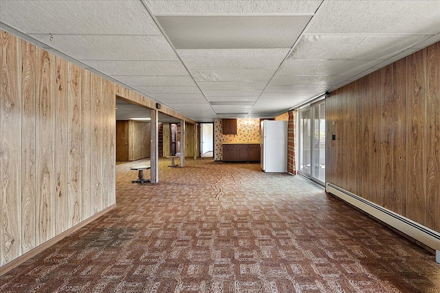 basement featuring wood walls, a drop ceiling, and baseboard heating