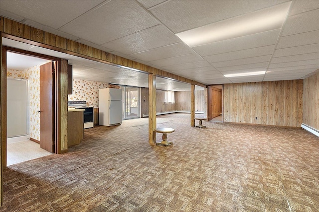 basement with freestanding refrigerator, wooden walls, baseboards, and a paneled ceiling