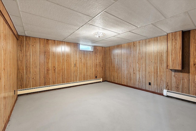 below grade area featuring wooden walls, a drop ceiling, and a baseboard radiator