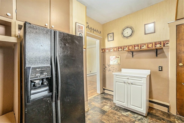 kitchen featuring baseboards, baseboard heating, black fridge, and stone finish flooring