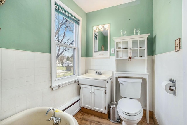 bathroom featuring tile walls, vanity, a freestanding tub, toilet, and a wainscoted wall