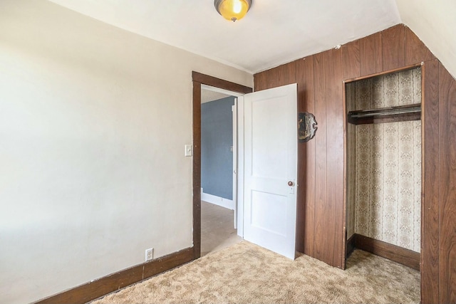 unfurnished bedroom featuring a closet, carpet, vaulted ceiling, wood walls, and baseboards