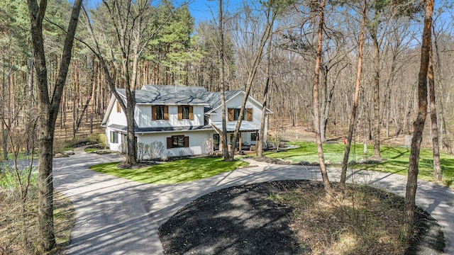 view of front of house featuring covered porch, driveway, a wooded view, and a front yard
