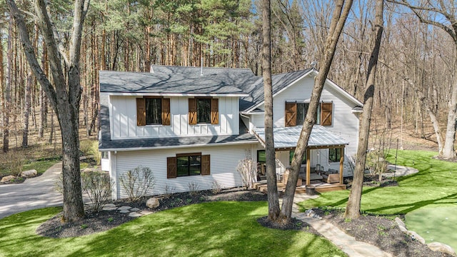 view of front of home featuring a front yard, a patio, a shingled roof, and board and batten siding