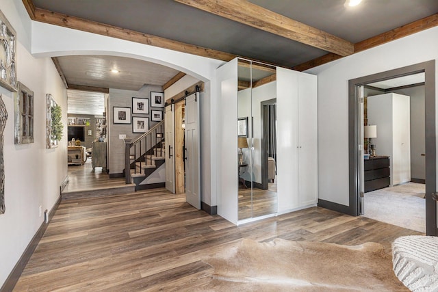 hall featuring wood finished floors, arched walkways, a barn door, baseboards, and beam ceiling