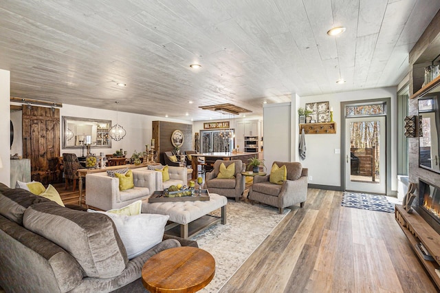 living area with light wood finished floors, recessed lighting, an inviting chandelier, and a glass covered fireplace