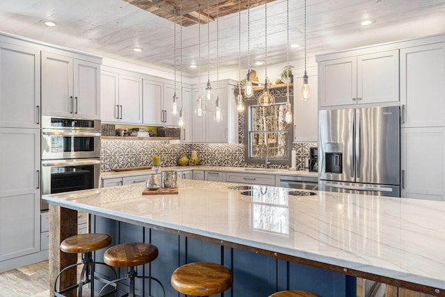 kitchen featuring light stone countertops, stainless steel appliances, a kitchen bar, and a sink