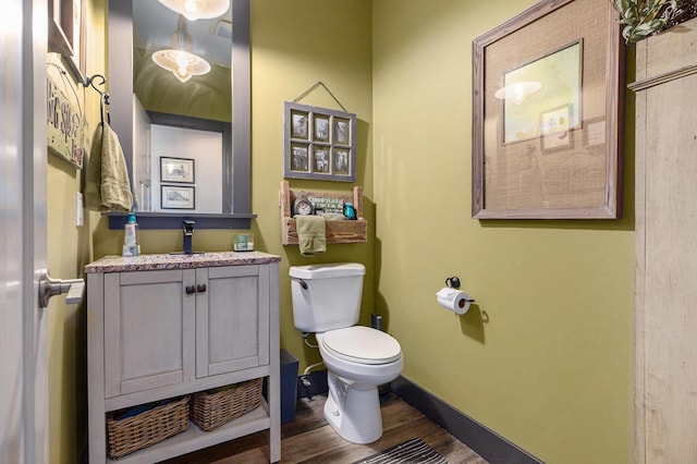 half bath featuring baseboards, wood finished floors, toilet, and vanity