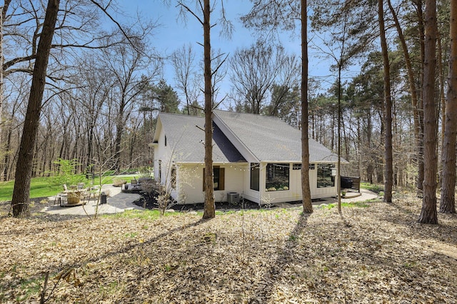 view of home's exterior featuring cooling unit, a shingled roof, and an outdoor fire pit