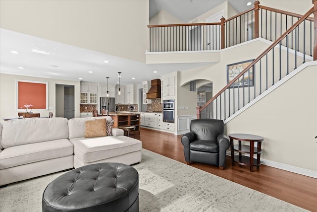 living room featuring dark wood-style flooring, arched walkways, stairs, a high ceiling, and recessed lighting
