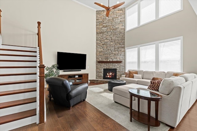 living area with ceiling fan, a towering ceiling, a fireplace, dark wood finished floors, and stairs