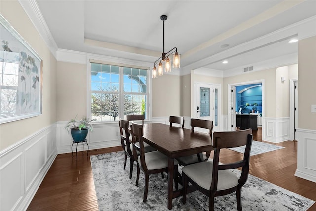 dining space featuring visible vents, a wainscoted wall, dark wood-style floors, ornamental molding, and a decorative wall