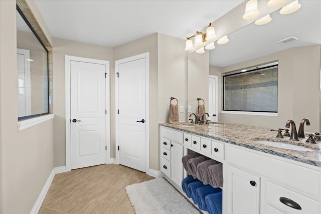 bathroom with double vanity, visible vents, a tile shower, a sink, and baseboards