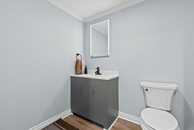 bathroom featuring wood finished floors, baseboards, vanity, toilet, and ornamental molding