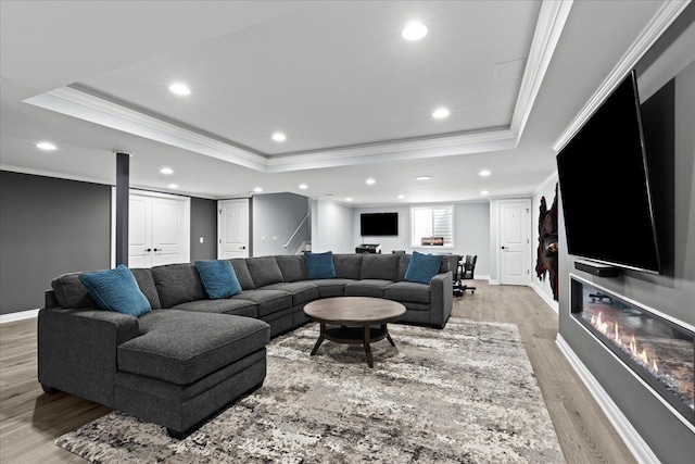 living room with crown molding, baseboards, recessed lighting, a raised ceiling, and light wood finished floors