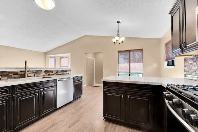 kitchen featuring appliances with stainless steel finishes, a sink, dark cabinets, tasteful backsplash, and vaulted ceiling