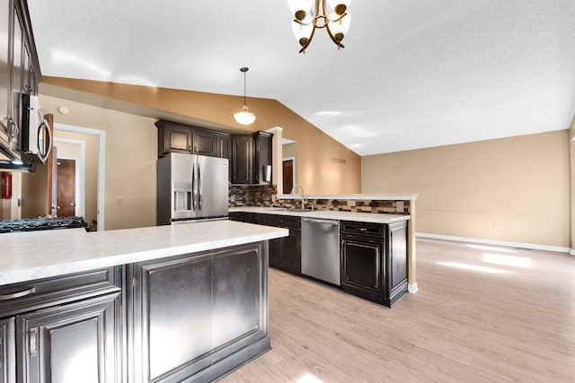 kitchen featuring backsplash, a sink, a peninsula, lofted ceiling, and stainless steel appliances
