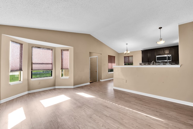 unfurnished living room featuring vaulted ceiling, light wood finished floors, a textured ceiling, and a chandelier