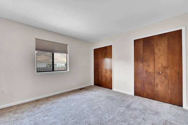 unfurnished bedroom with two closets, baseboards, visible vents, and carpet floors