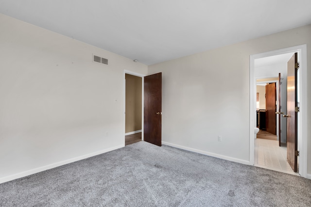 unfurnished bedroom with visible vents, baseboards, ensuite bathroom, and light carpet