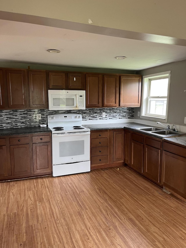 kitchen featuring white appliances, decorative backsplash, light wood finished floors, and a sink