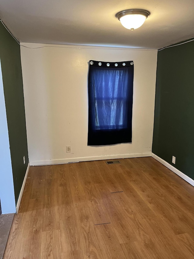 unfurnished room featuring visible vents, wood finished floors, and baseboards