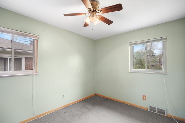 carpeted spare room featuring baseboards, visible vents, and ceiling fan