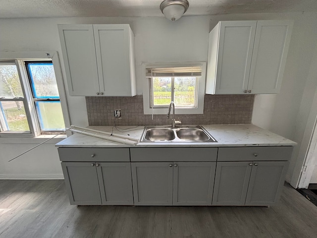 kitchen featuring light stone countertops, a sink, light wood-style floors, tasteful backsplash, and gray cabinetry