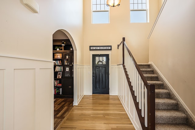 entrance foyer featuring a towering ceiling, arched walkways, stairway, and wood finished floors