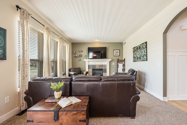 living area with baseboards, arched walkways, a tile fireplace, and carpet floors