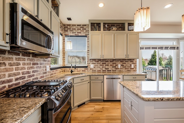 kitchen with light stone countertops, decorative light fixtures, light wood-style floors, appliances with stainless steel finishes, and a sink