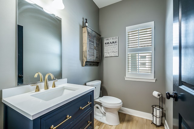 half bath featuring wood finished floors, toilet, vanity, and baseboards